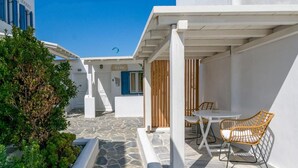 A white building with a stone pathway leading to a covered outdoor seating area with a table and chairs. - Gelos House (Mykonos)