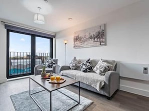 A modern living room with a sofa, coffee table, and a view of a swimming pool. - Modern 2BR City Centre Stay Near Hospital (Liverpool)