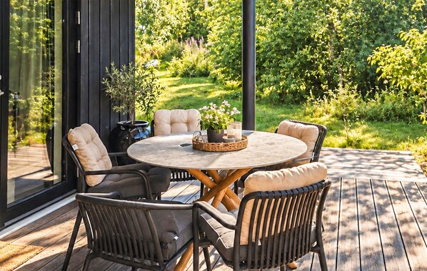 En udendørs terrasse med et rundt bord, polstrede stole og en potteplante.