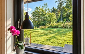 A window with a view of a grassy yard and trees, a hanging lamp, and a potted plant with pink flowers. - 3 bedroom gorgeous home in Ejstrupholm (Ejstrupholm)