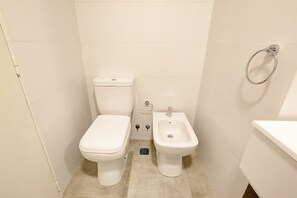 Et lille, kompakt badeværelse med toilet, bidet og et håndklædetørrestativ.