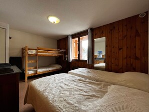 Una habitació amb lliteres, escriptori i finestra amb cortines.