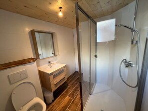 Een moderne badkamer met een houten wastafelmeubel, een douchecabine met glazen wanden en een toilet.