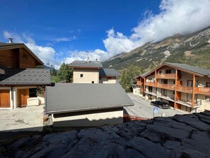 Un lodge de montaña con varios balcones, un camino pavimentado y vistas de las montañas circundantes.