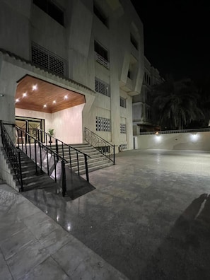 Un edificio con una escalera que lleva a una entrada, un área techada con techo de madera y un patio empedrado.