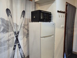 A white refrigerator with a black microwave on top, a pair of skis leaning against the wall, and a door with a curtain. - Studio for 4, South facing (Valloire)