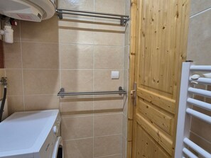 A bathroom with a white washing machine, a wooden door, and a tiled wall. - Studio for 4, South facing (Valloire)
