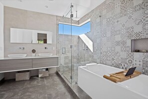 A modern bathroom with a glass-enclosed shower, a large bathtub, and a vanity with two sinks.