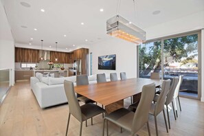 A modern kitchen with wooden cabinets, a dining area with a wooden table and chairs, and a large window offering a view of the outdoors.