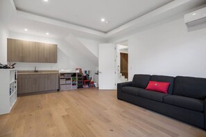 Een modern appartement met keuken, een zithoek met een zwarte bank en een rode kussens, houten vloeren en witte muren.