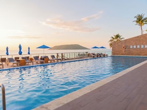 Una piscina con lettini e ombrelloni, un muro in mattoni e vista sul mare.