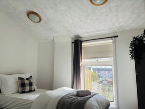 Quarto com cama, janela com cortinas, vista de edifícios e luminária circular no teto.