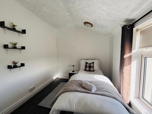 Quarto com cama, mesas de cabeceira, janela com cortinas e prateleiras fixadas na parede com plantas.