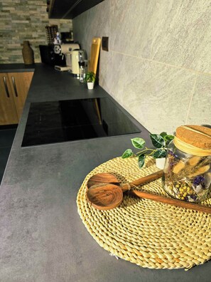 Eine Küche mit einer schwarzen Arbeitsplatte, Holzkochern, einer gewebten Tischmatte und einem Glas mit getrockneten Blumen.