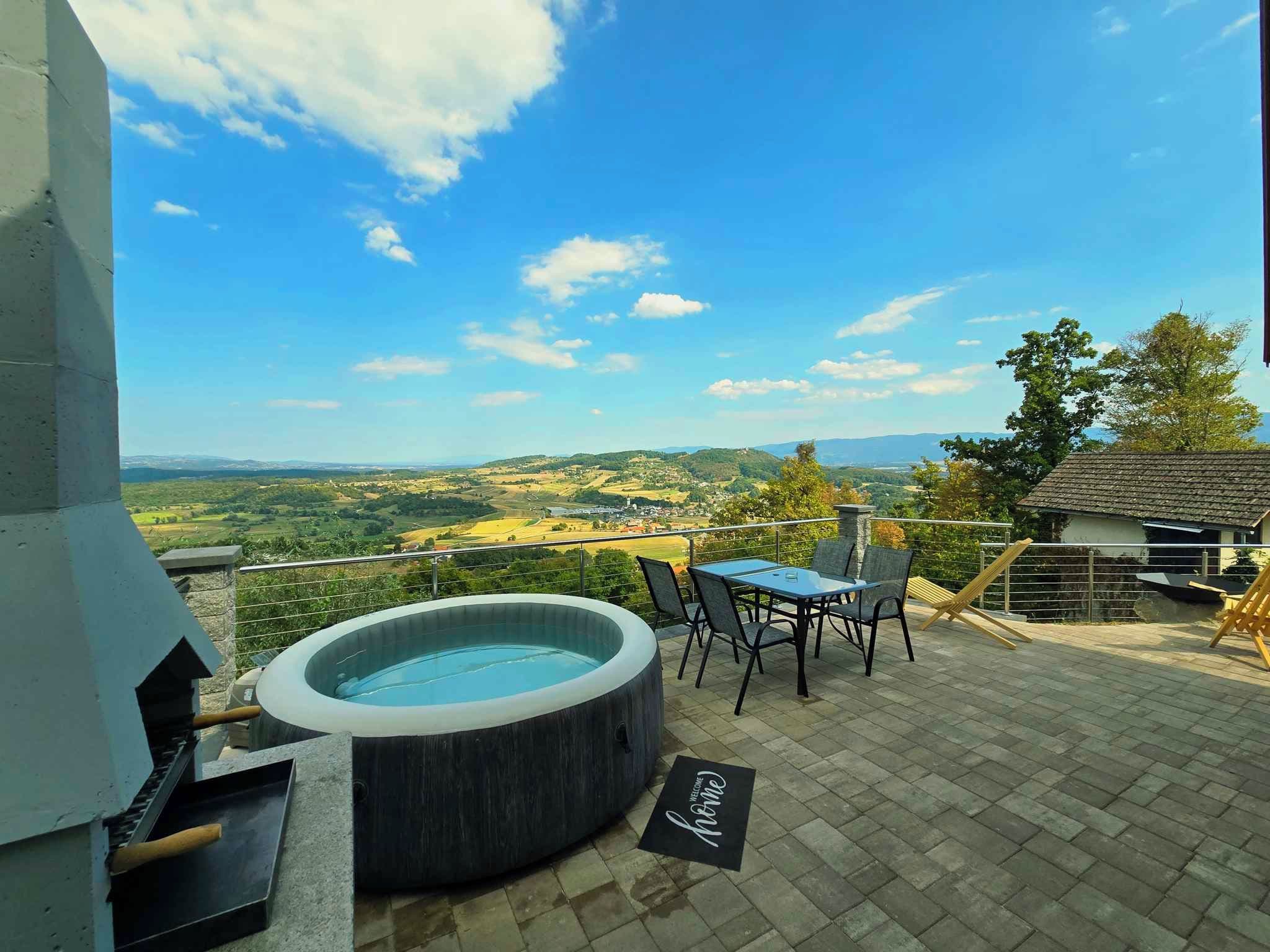 Un jacuzzi en un patio con mesa y sillas, con vistas a un paisaje pintoresco.