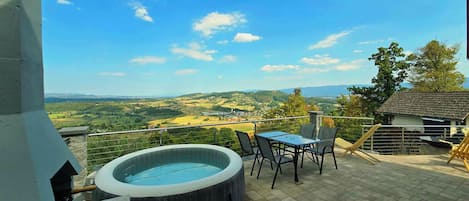 Un jacuzzi en un patio con mesa y sillas, con vistas a un paisaje pintoresco.