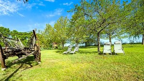 Un espacio al aire libre con césped, un columpio de madera y dos tumbonas.