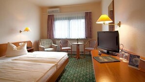 Una habitación de hotel con cama, televisión, escritorio con lámpara y ventana con cortinas.