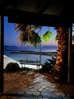 A stone pathway leading to a bench overlooking a beach with palm trees and a view of the sea.