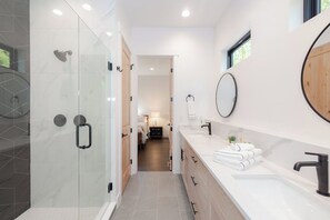 Un bagno moderno con box doccia in vetro, uno specchio grande e un mobile lavabo bianco con rubinetto nero.