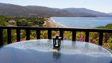 A glass table with a lantern on it, overlooking a beach and mountains.