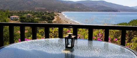 A glass table with a lantern on it, overlooking a beach and mountains.