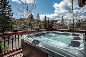 Ein Whirlpool auf einer Terrasse mit Metallgeländer, umgeben von Bäumen und Gebäuden.