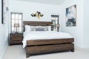 A bedroom with a wooden bed, two bedside tables, a wall-mounted light fixture, and a large abstract painting. - Apres Chalet | Pet Friendly | Downtown House | Private Hot Tub (Winter Park)