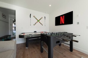 Ein Zimmer mit einem Kicker, einem Billardtisch und einem an der Wand befestigten Fernseher.