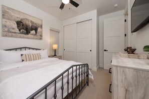 Ein Schlafzimmer mit einem Bett, einem Nachttisch, einer Lampe, einem Bison-Gemälde und einem Kleiderschrank.