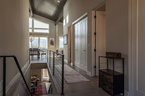 Ein geräumiger Flur mit einer Treppe, die zu einem Balkon führt, einer Holzbalkendecke und Blick ins Freie.