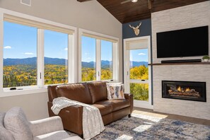 Ein Wohnzimmer mit einer braunen Ledersofa, einem Kamin und großen Fenstern mit Blick auf eine Berglandschaft.