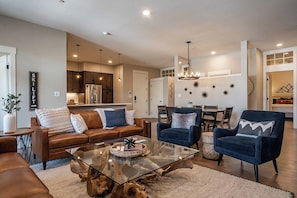 A modern living room with a glass coffee table, leather sofas, and a dining area with a chandelier. - Hideaway Haven | Tucked Away | Near Downtown (Winter Park)