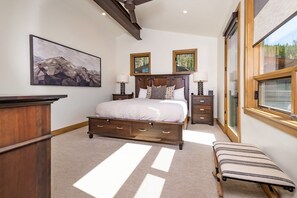 Ein Schlafzimmer mit einem großen Bett, Nachttischen, einer Bank, einem Gemälde und einem Fenster.