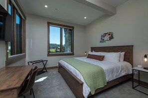 A bedroom with a large bed, a desk, and a chair. There is a window providing a view of the outdoors. - Vista Vogue | Hot Tub & Panoramic Views | Downtown (Fraser)