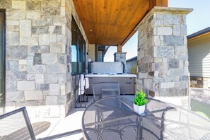 An outdoor patio with a stone wall, a wooden ceiling, a hot tub, and a round metal table with a potted plant. - Vista Vogue | Hot Tub & Panoramic Views | Downtown (Fraser)