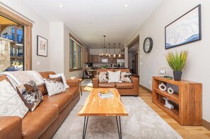 A modern living room with a brown leather sofa, a wooden coffee table, and a wooden console table with decorative items. - Vista Vogue | Hot Tub & Panoramic Views | Downtown (Fraser)