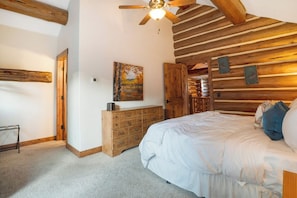 Une chambre avec un plafond en bois, un lit, une commode et un tableau accroché au mur.