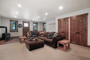 A living room with a sectional sofa, wooden side tables, a fireplace, and large wooden doors.