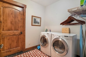 Une buanderie équipée de deux machines à laver à chargement frontal, d’une porte en bois, d’un tableau encadré accroché au mur et d’un étendoir à linge.