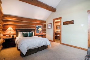 A log cabin bedroom with a large bed, wooden headboard, and a nightstand with a lamp. - Moose Drool Lodge | Luxury Mountain Lodge | Private Hot Tub (Winter Park)