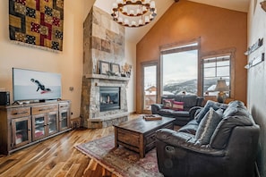 A living room with a stone fireplace, leather sofa, and a television. - Hygge Hideaway | Private Hot Tub (Winter Park)