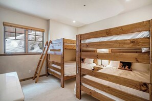 Une chambre avec des lits superposés, une fenêtre donnant sur un paysage enneigé et une échelle.
