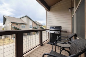Ein Balkon mit Grill, Stühlen und Blick auf benachbarte Gebäude.