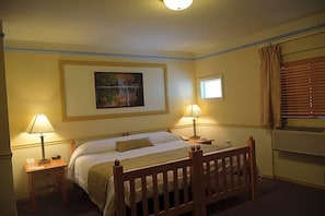 A hotel room with a bed, two bedside tables, a nightstand, a wall-mounted artwork, a window with curtains, and an air conditioning unit. - Wonder Valley Ranch Resort and Conference Center (Sanger)