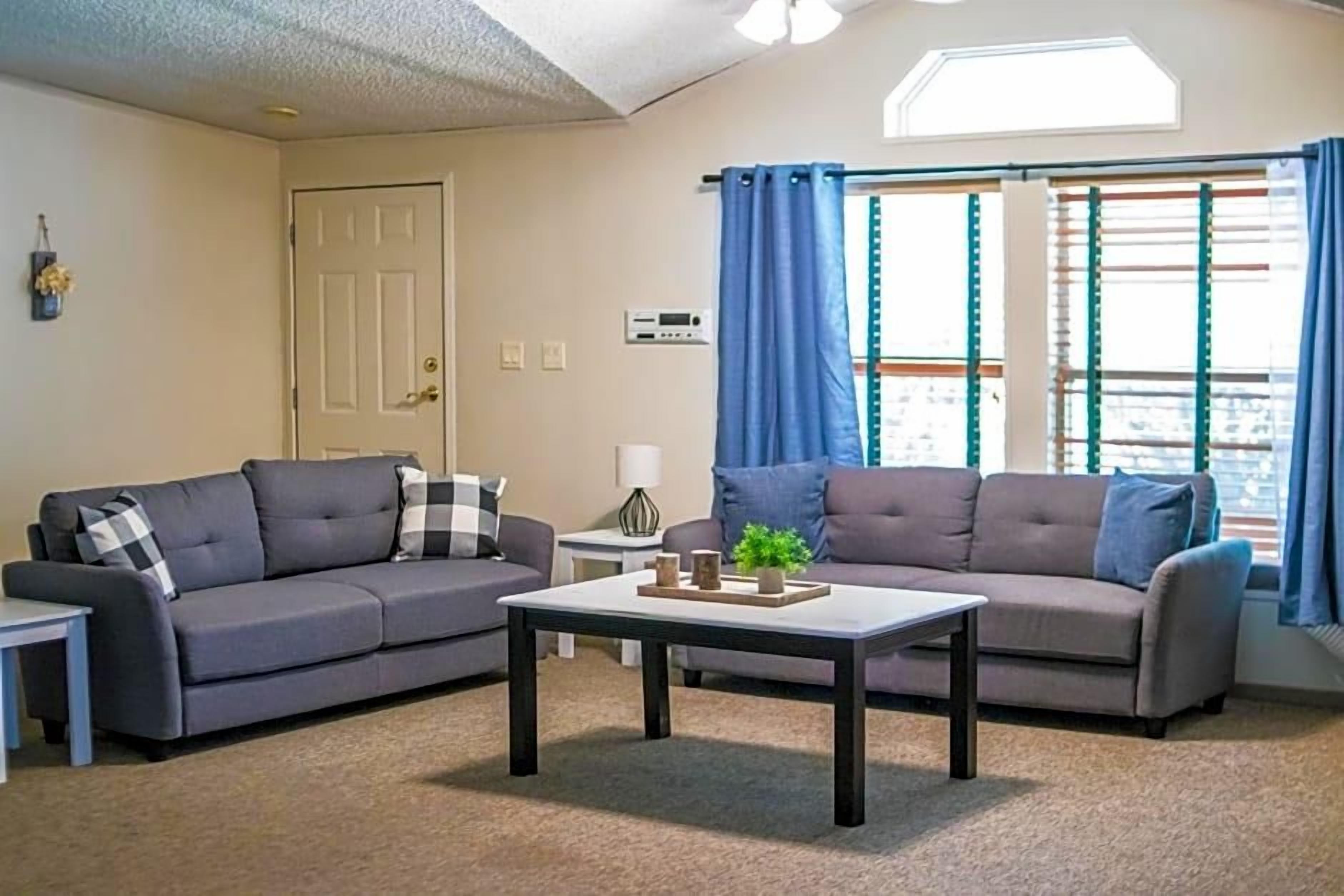 A living room with two sofas, a coffee table, a door, and a window with curtains.