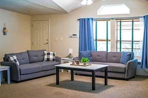A living room with two sofas, a coffee table, a door, and a window with curtains. - Wonder Valley Ranch Resort and Conference Center (Sanger)