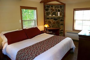A bedroom with a bed, a nightstand, a lamp, a stone wall, and a window. - Wonder Valley Ranch Resort and Conference Center (Sanger)