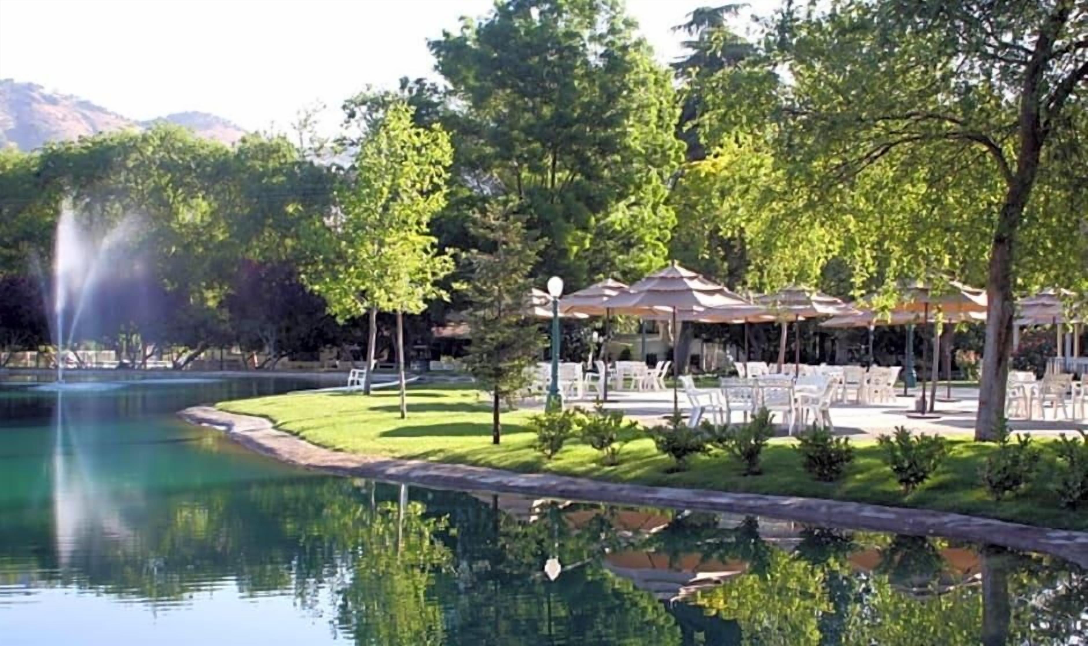A tranquil outdoor setting with a pond, trees, and outdoor seating areas.