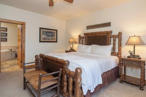 A bedroom with a large bed, wooden headboard, two bedside tables with lamps, a chair, a framed picture, and a sign above the bed. - Lakota Majesty | Pet Friendly | Hot Tub | Sauna | Across From Resort (Winter Park)